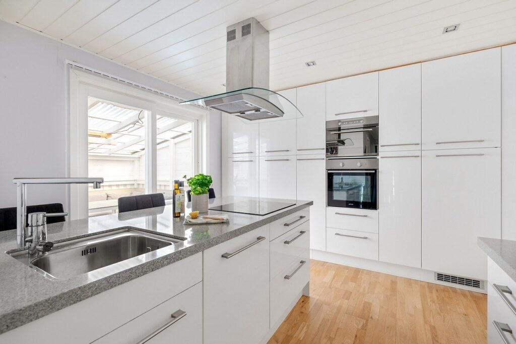 A white kitchen with an island that contains the sink and hob.  The hob extractor fan or cooker hood is hanging from the ceiling.
